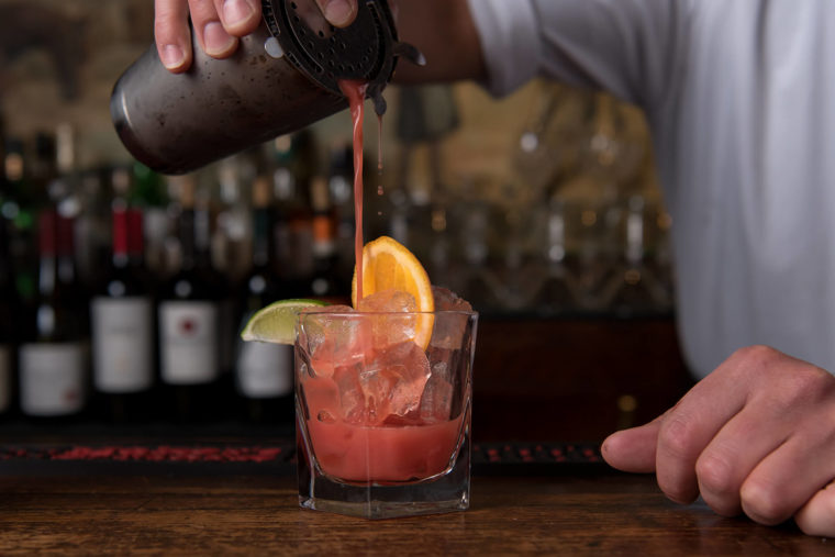 Bartending pouring a cocktail from a shaker into a glass.