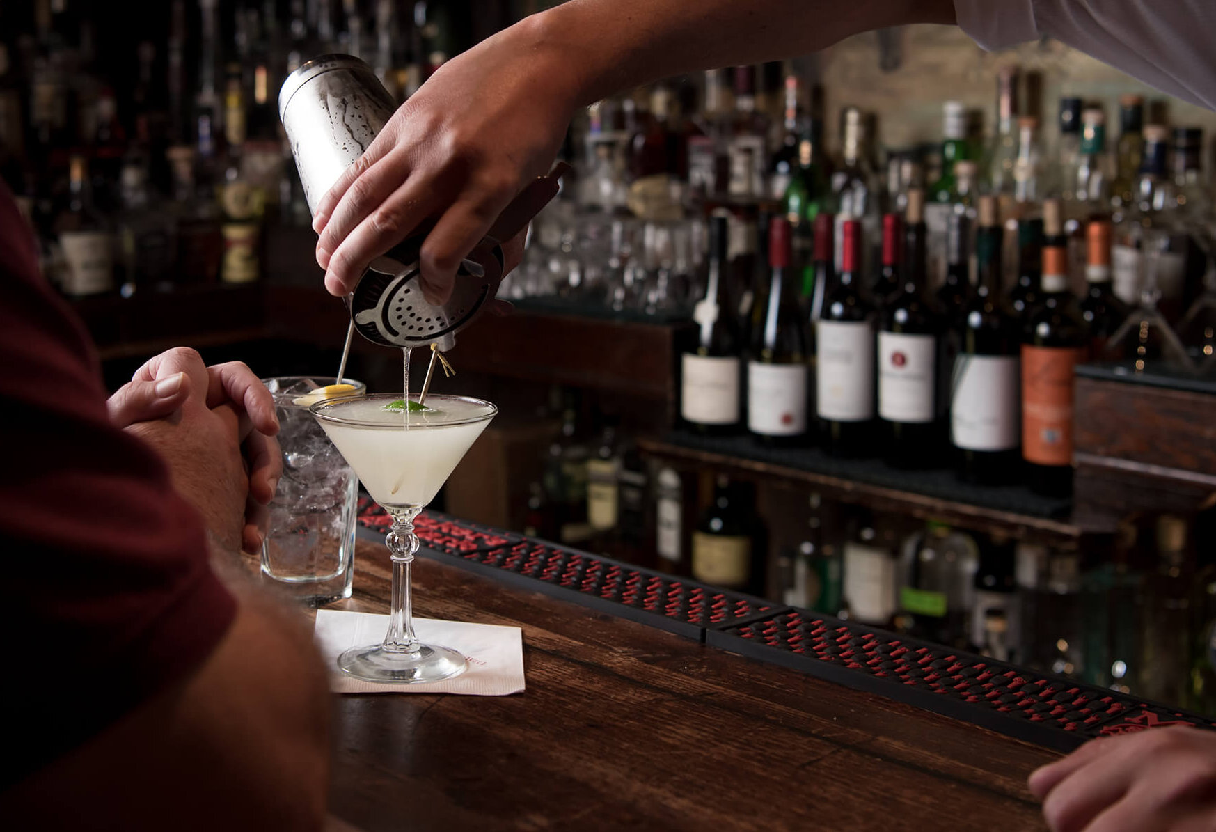 Bartender pouring a cocktail into a martini glass.