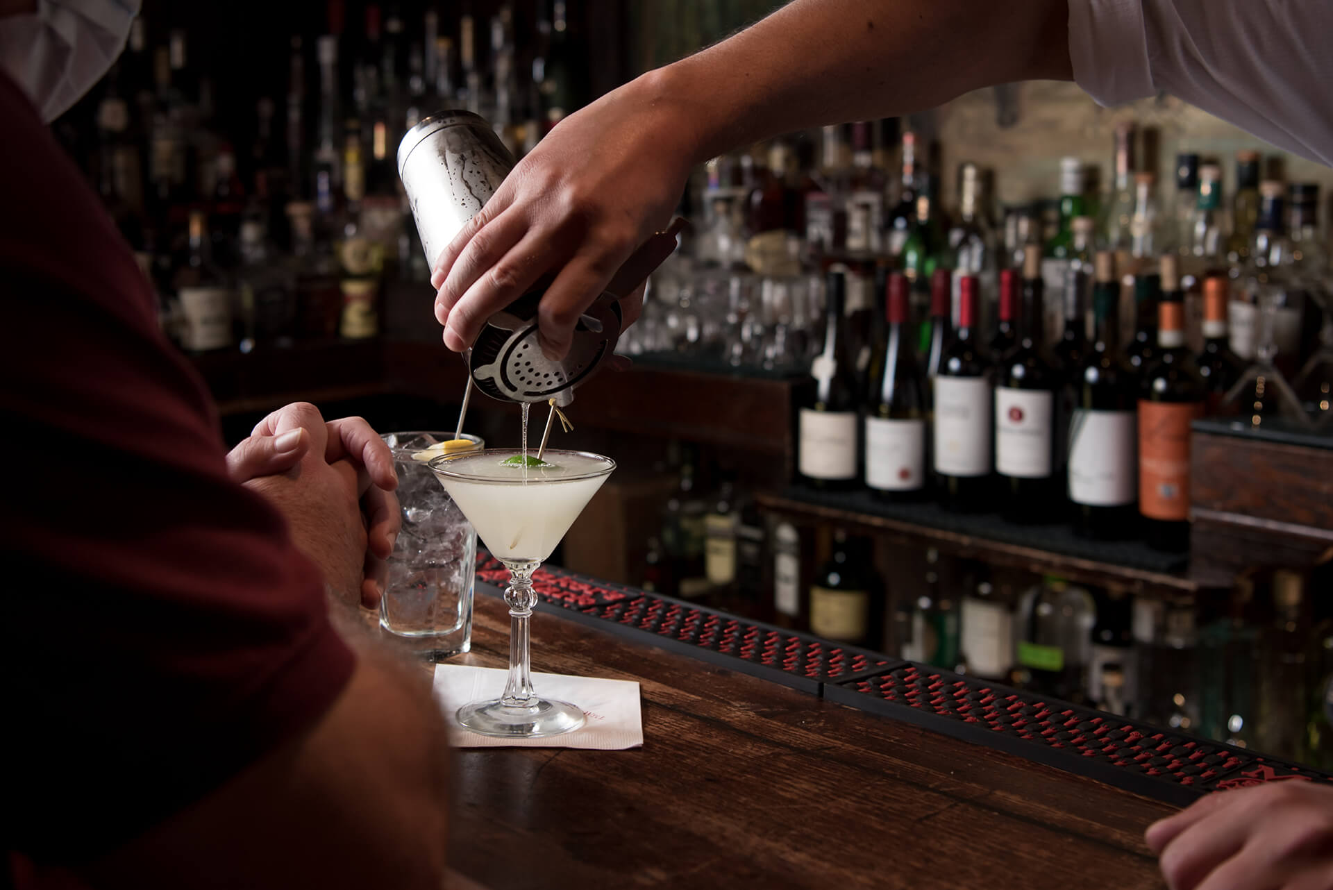 Bartender pouring a cocktail into a martini glass.