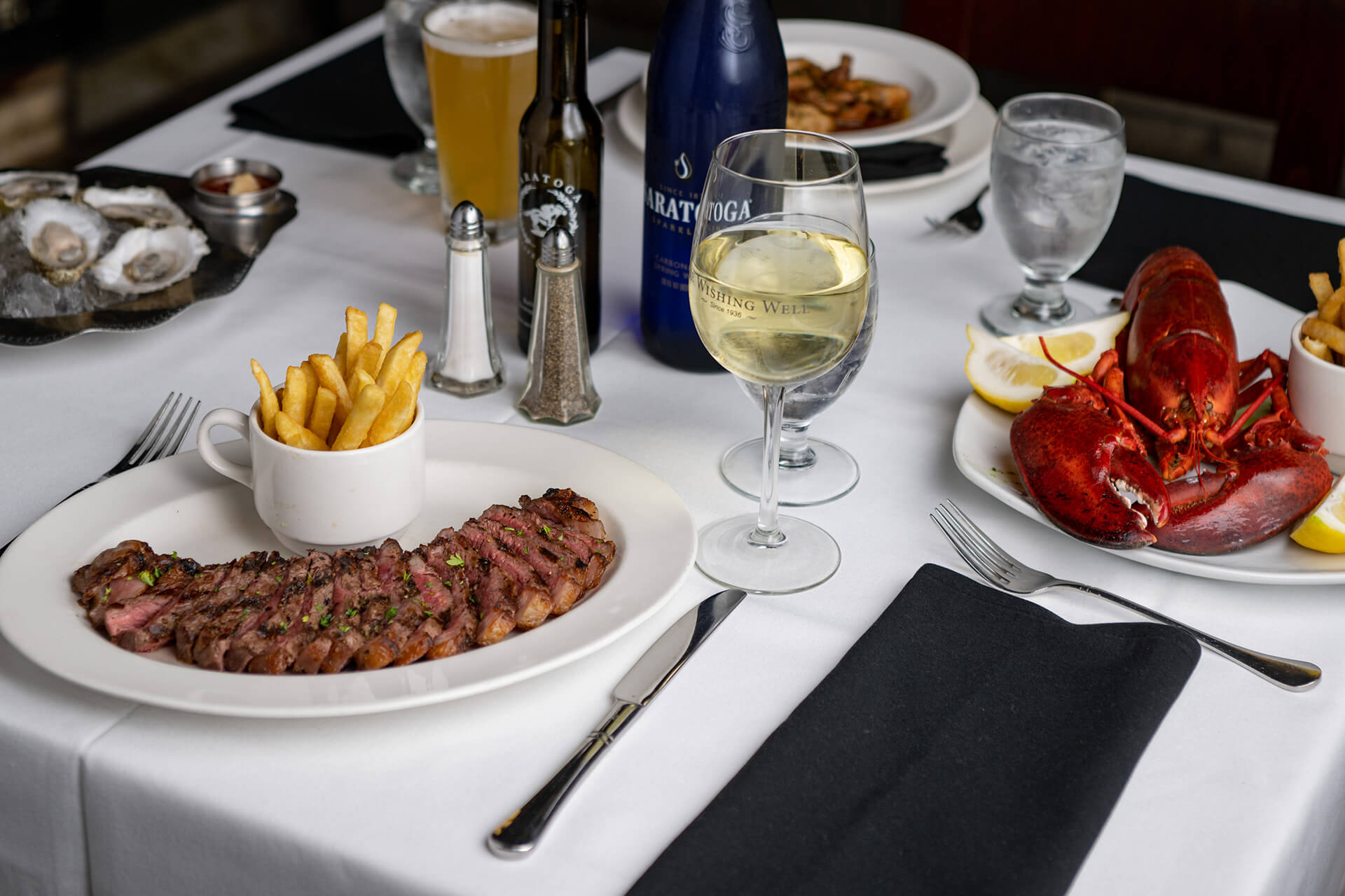 Dining table with a plate of steak, lobster, wine and beer glass.