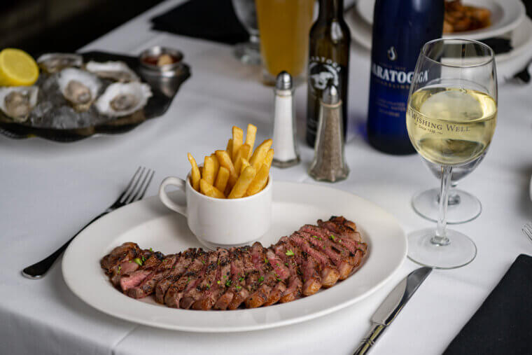 Seared steak sliced evenly and lined up along a plate with a teacup of frites.